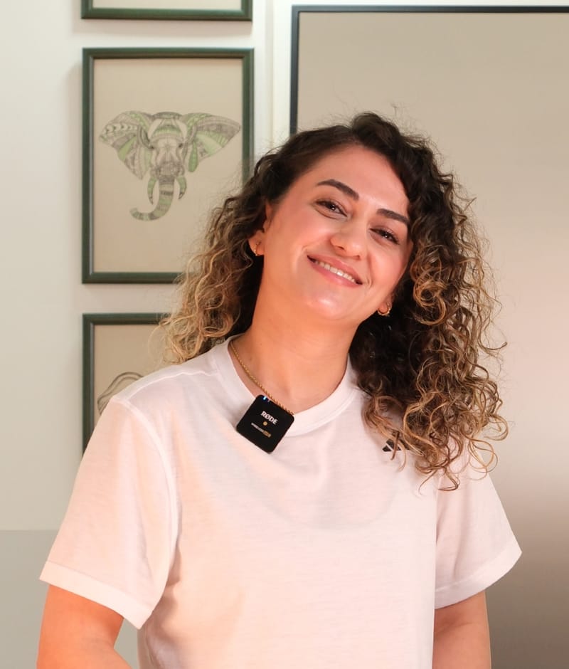 Poseidon Pilates eğitmeni Kübra Taş Basmaz, stüdyoda beyaz tişörtle gülümseyerek kameraya bakıyor.