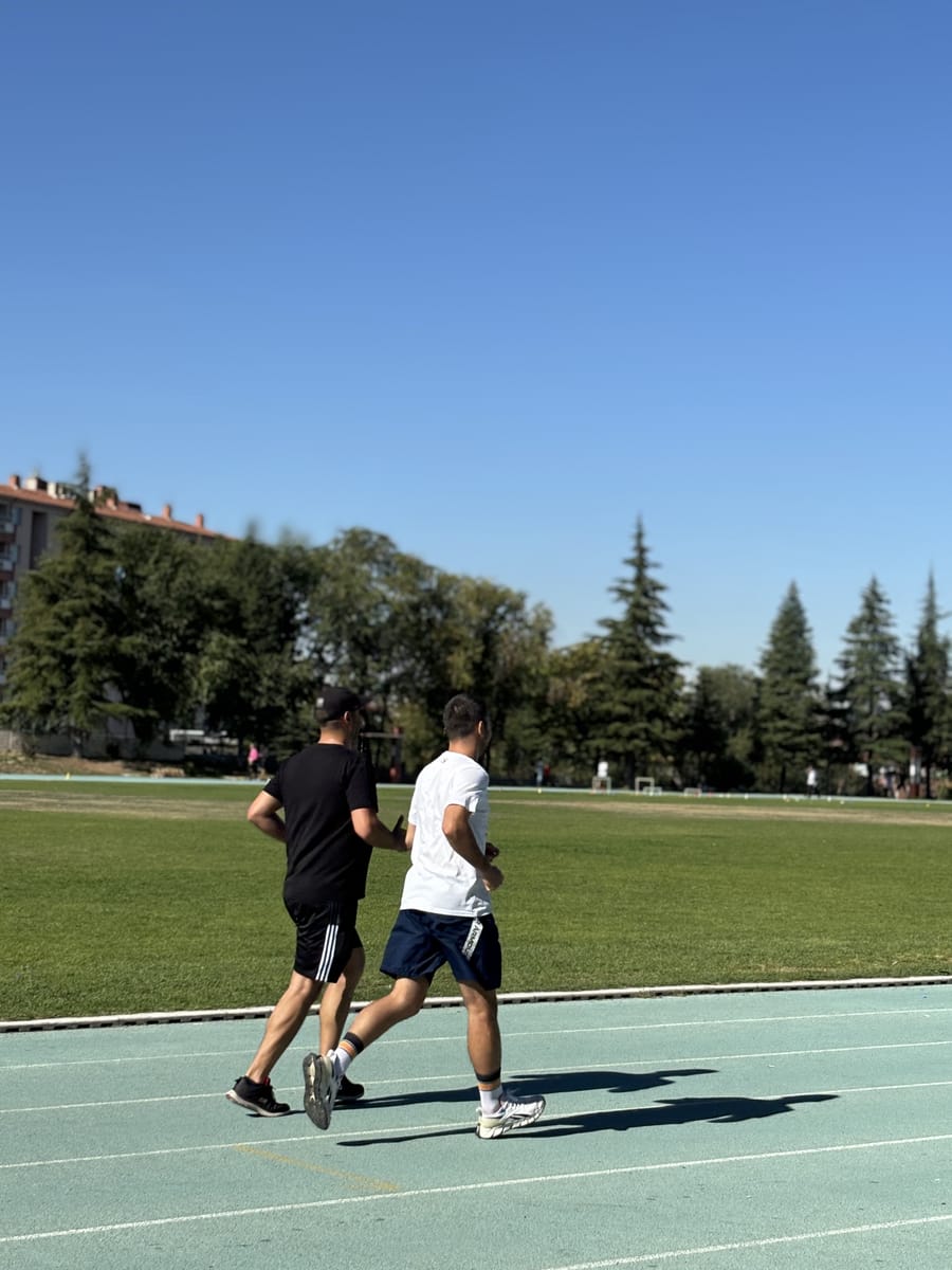 Atletizm pistinde yan yana hafif tempoda koşan iki katılımcı.